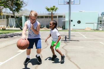 Two young kids, a boy and a girl, enthusiastically play basketball together, showcasing their active and energetic nature. They engage in the sport, dribbling the ball, and showcasing their athleticism while exercising their muscles. The image captures their joyful spirit and dedication to physical activity and teamwork.